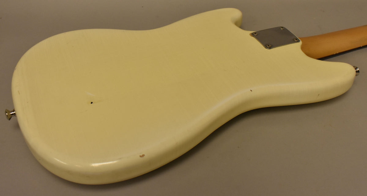 The back of an Olympic White Mustang guitar, showing a worn nitro finish, a chrome neck plate, and a few small dings.