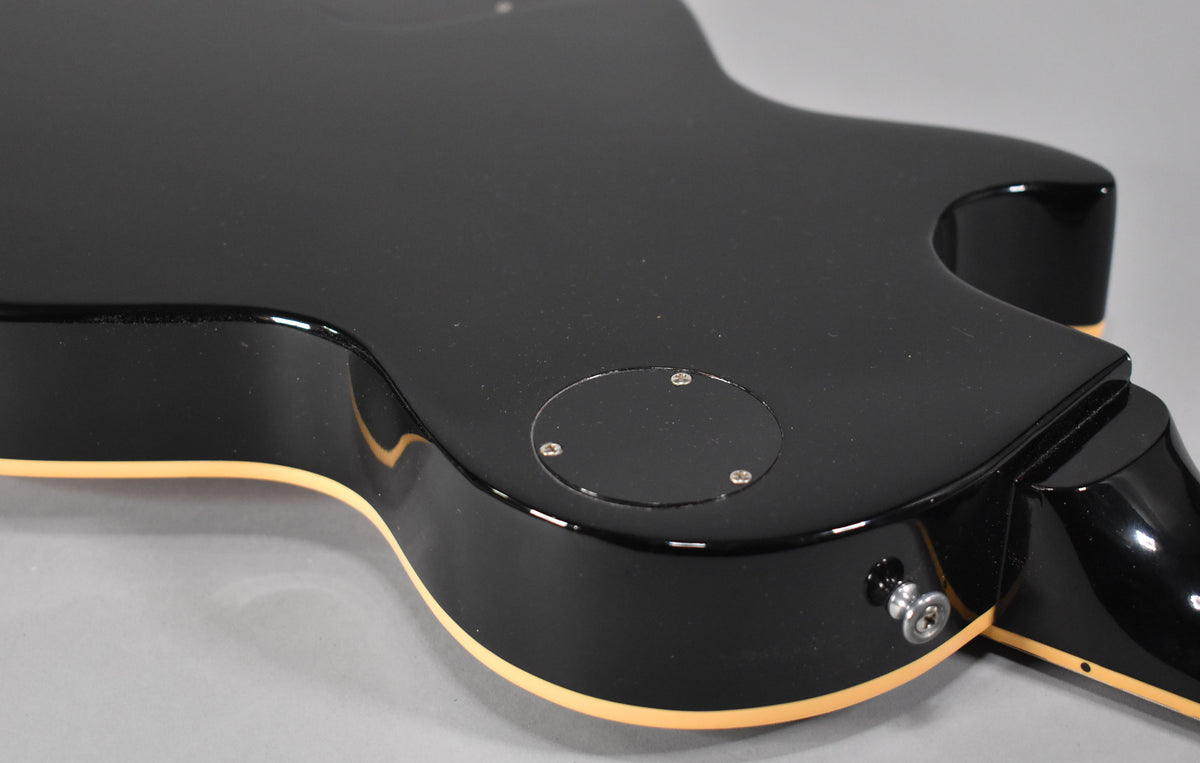 The guitar's glossy black back, with cream binding, shows a circular control cavity cover and a chrome output jack.