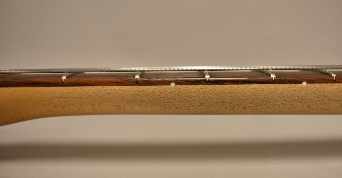 Close-up of the guitar's neck, showing the dark rosewood fretboard with white dot markers and a light wood neck with a textured finish.