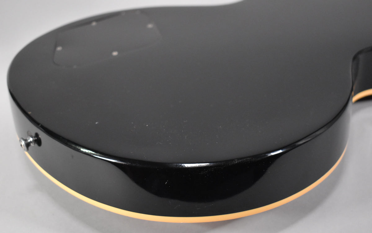 The guitar's black back and side are visible, with cream binding along the bottom edge and a strap button on the lower bout.