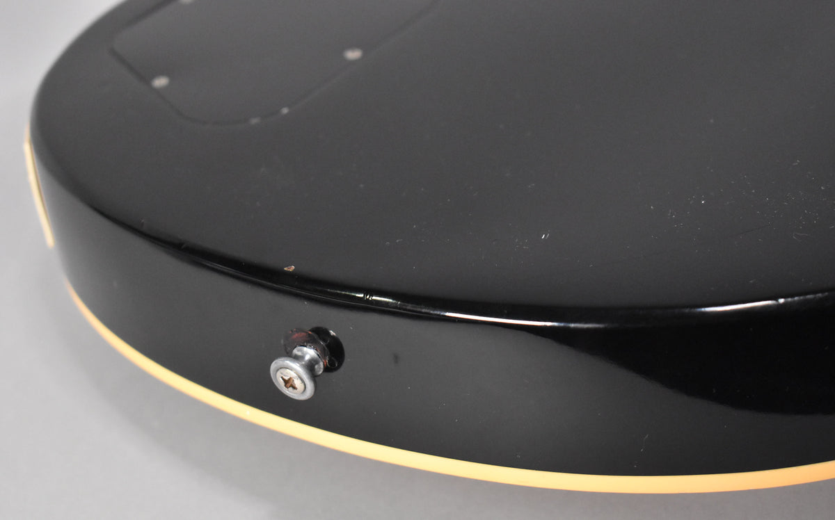 Close-up of the guitar's black glossy body with cream binding, showing the chrome output jack and light surface wear.