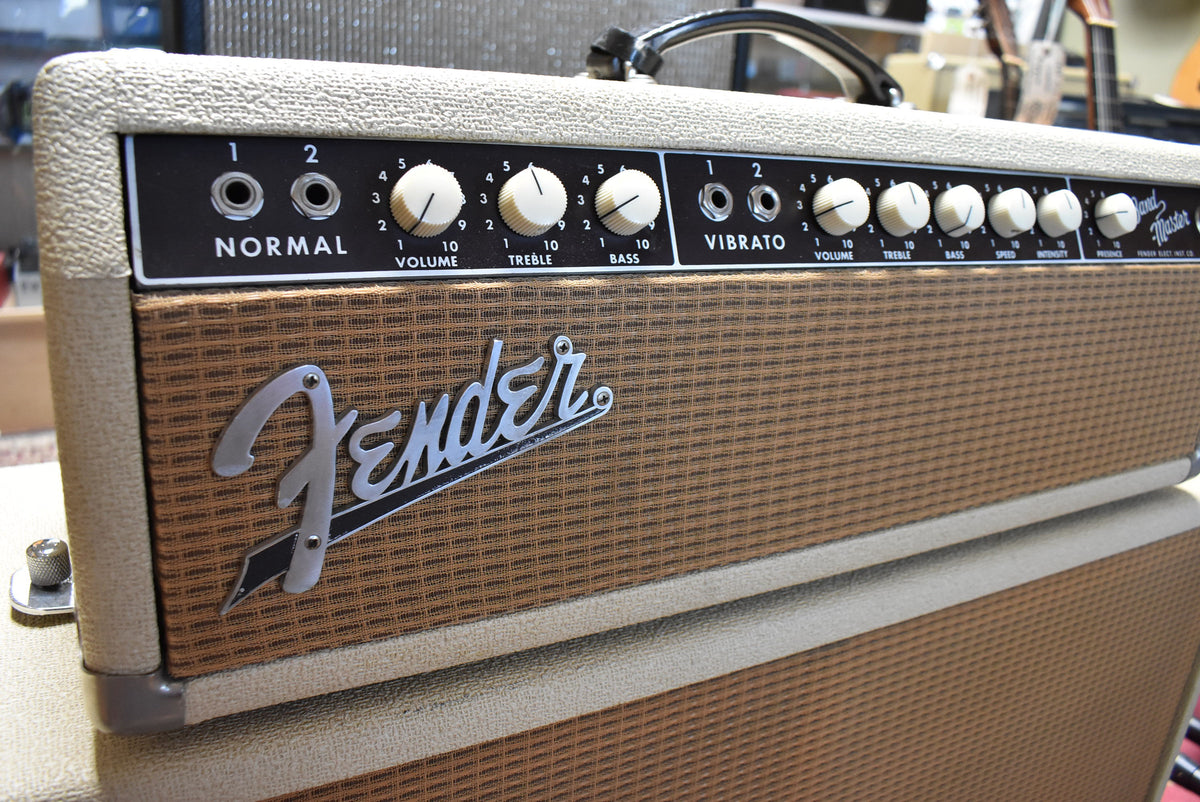 The blond amp head, seen from a high angle, has a brown grille cloth and a black control panel with white knobs and a black handle.