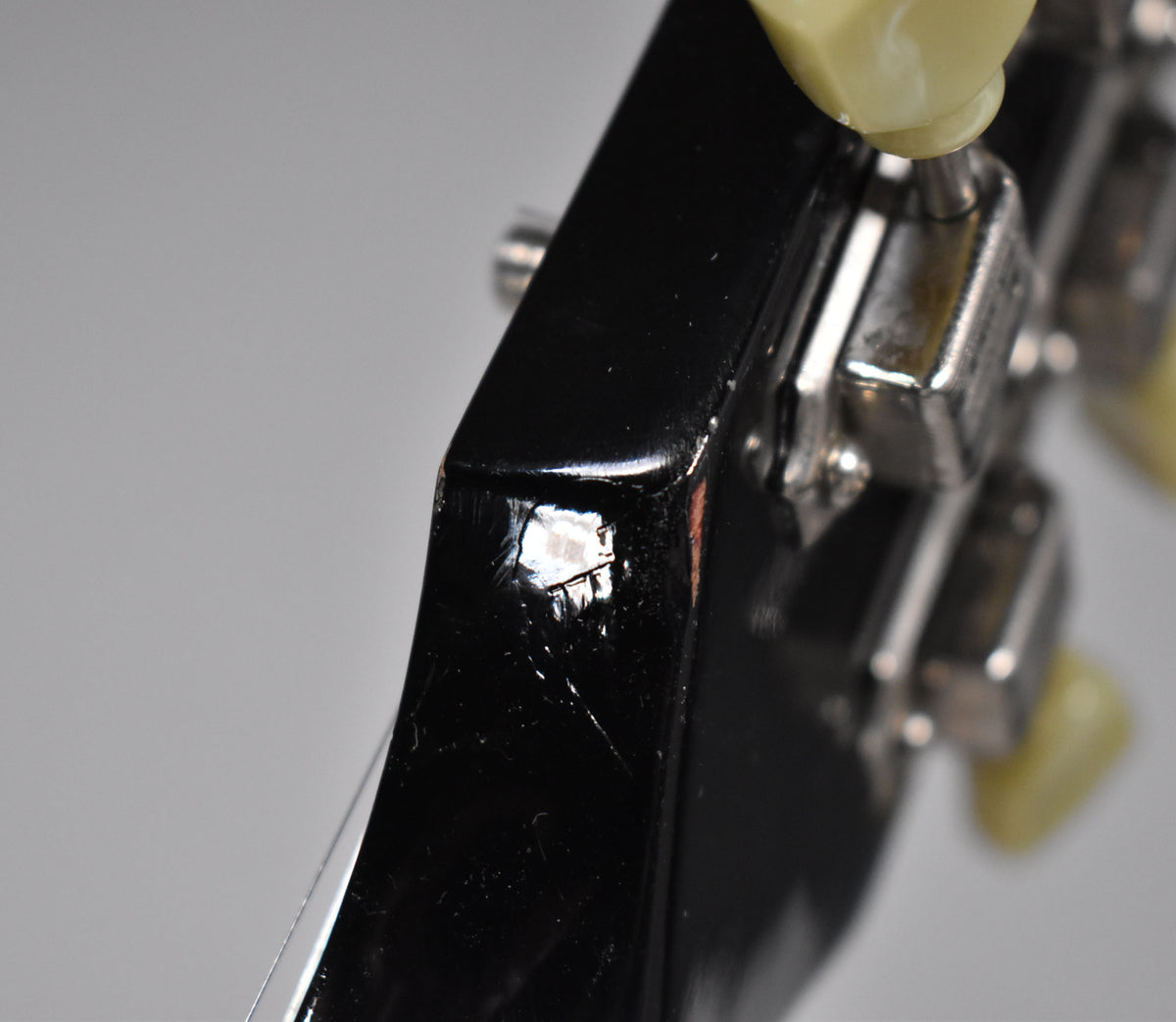 Close-up of the black headstock's edge, showing a large chip in the finish and many fine scratches near the chrome tuning pegs.