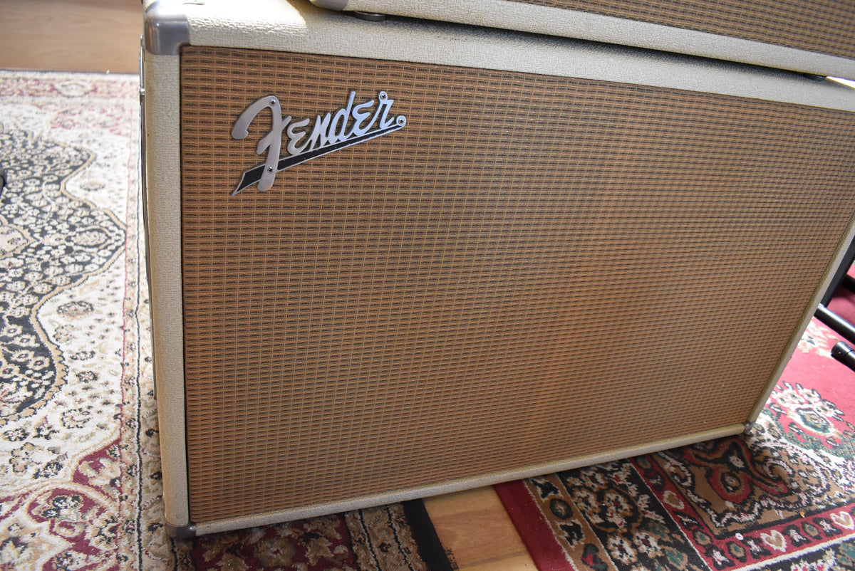 The blond 2x12 cabinet is angled from the left, showing its tan grille cloth and a silver logo, with minor scuffs on the corners.