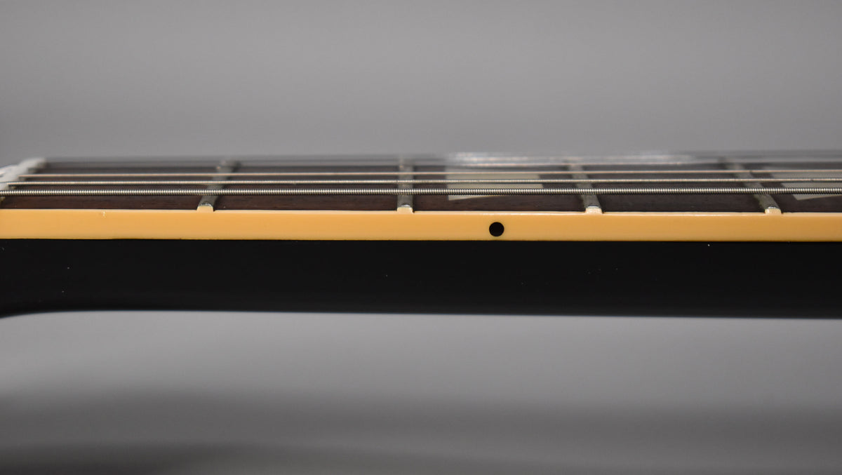Close-up of the guitar's neck from the side, showing the dark fretboard, light binding, and a single black dot inlay.