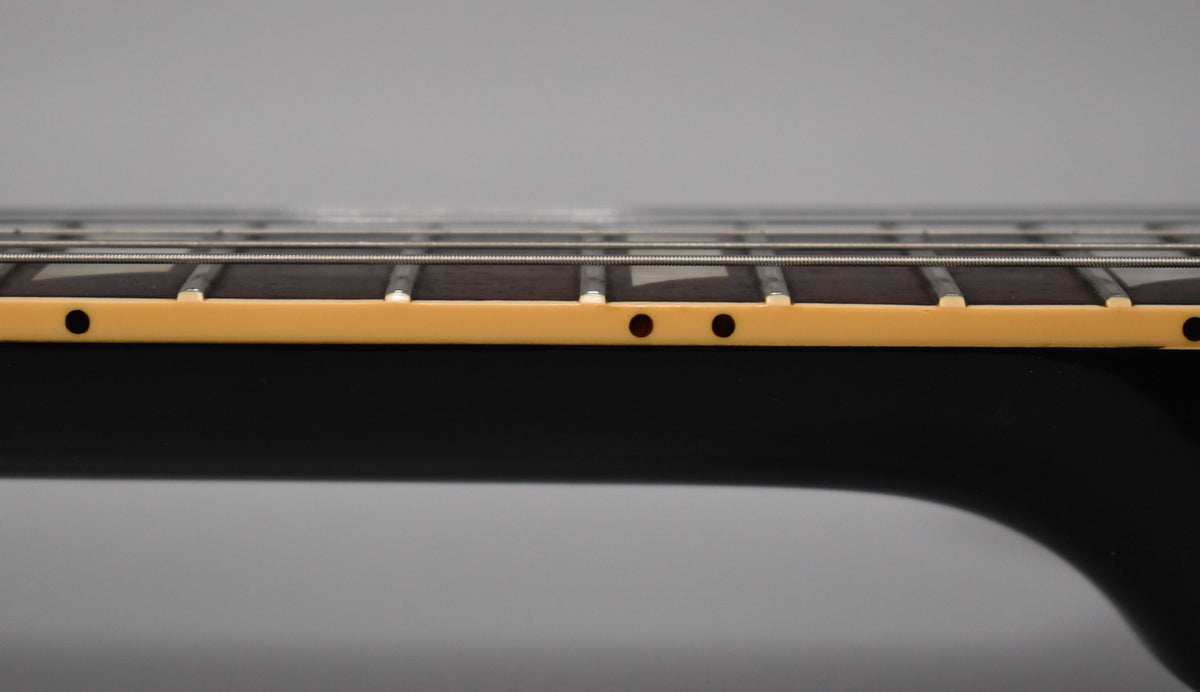 Close-up of the guitar's dark fretboard and light binding, showing frets, strings, and two small dark side dot markers.