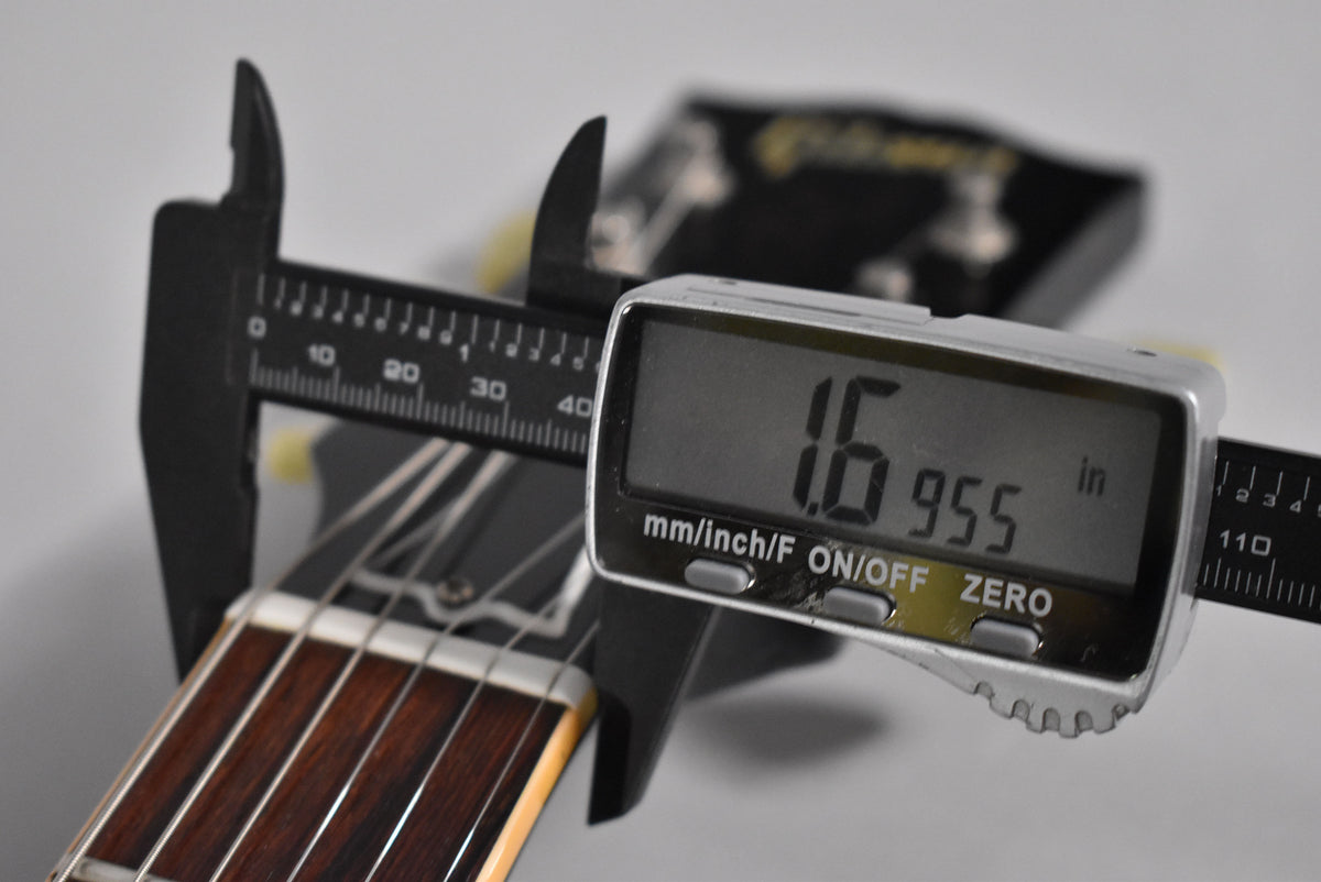 A digital caliper measures the guitar's nut width at 1.6955 inches, with the dark rosewood fretboard visible.