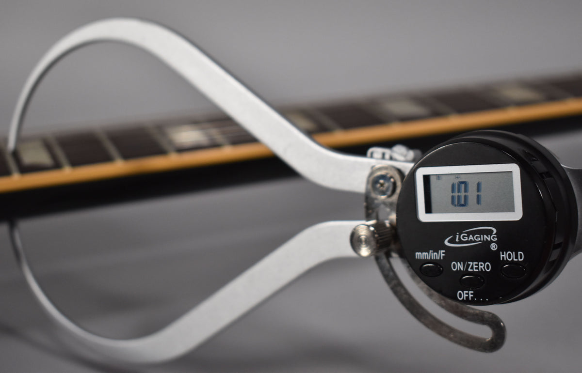 A digital caliper measures the guitar's neck thickness at 1.01 inches, with the fretboard and frets visible.