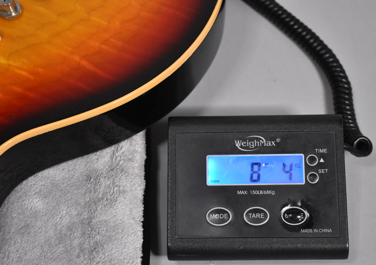Close-up of the guitar's lower bout with a Tri-Burst finish and cream binding, next to a digital scale displaying "8 lbs 4 oz".