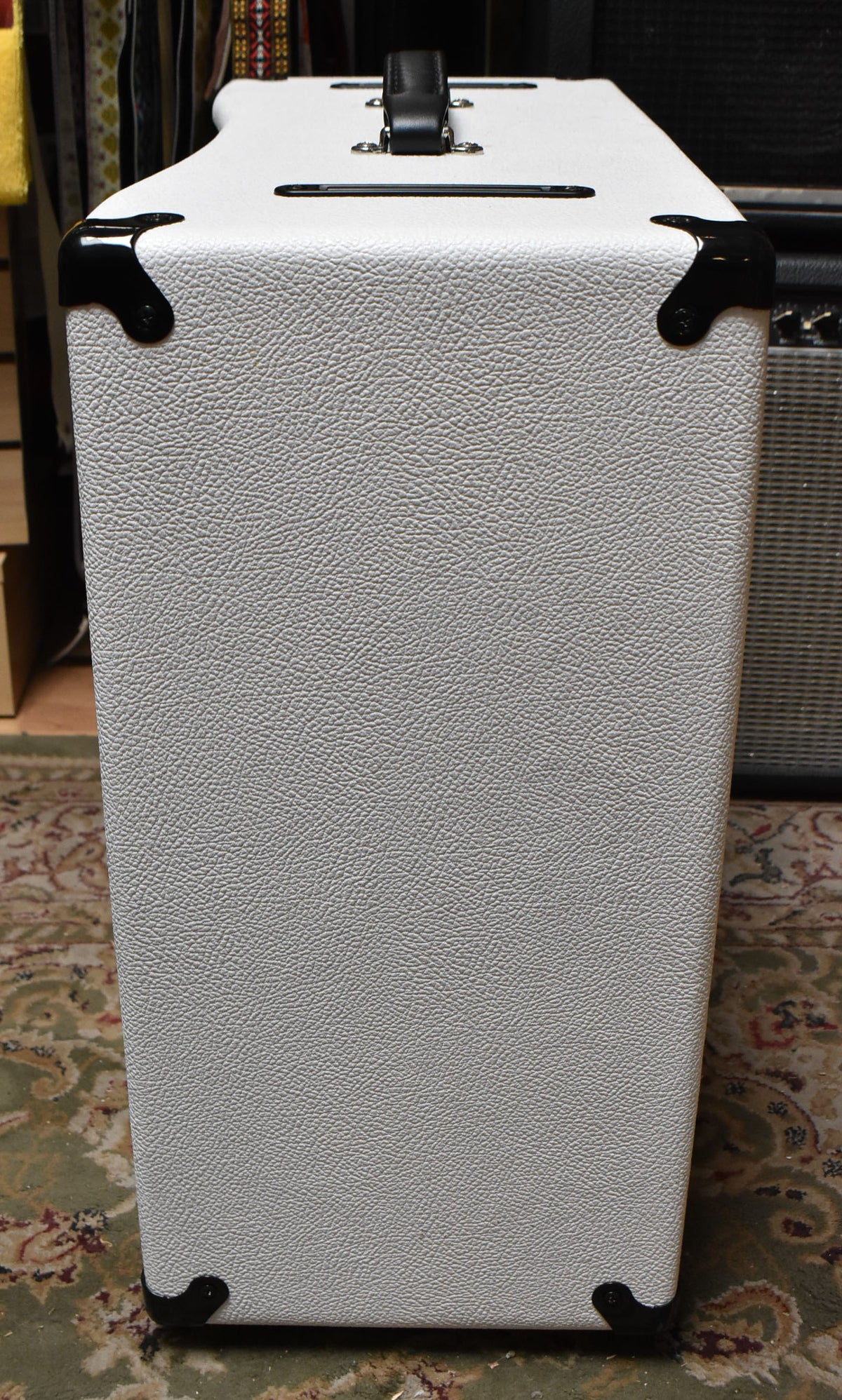 The white textured amplifier is viewed from the right side, showing a black handle and corner protectors on the top and bottom.