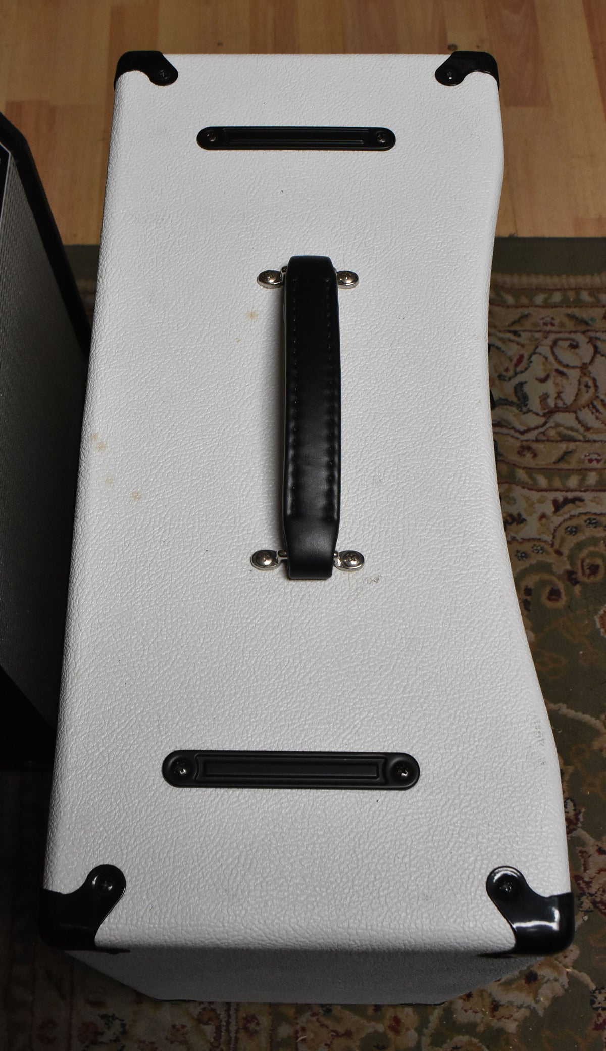Top-down view of the white textured amp with black corner protectors, a black leather handle, and two black vent grilles.