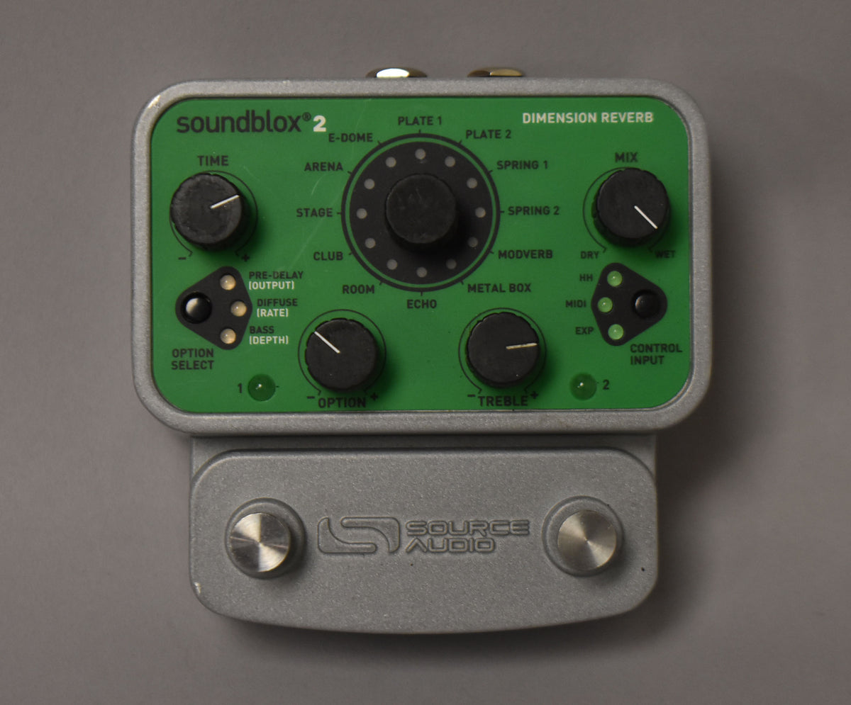Top-down view of a green and silver pedal with five black knobs, two black rocker switches, and two silver footswitches.