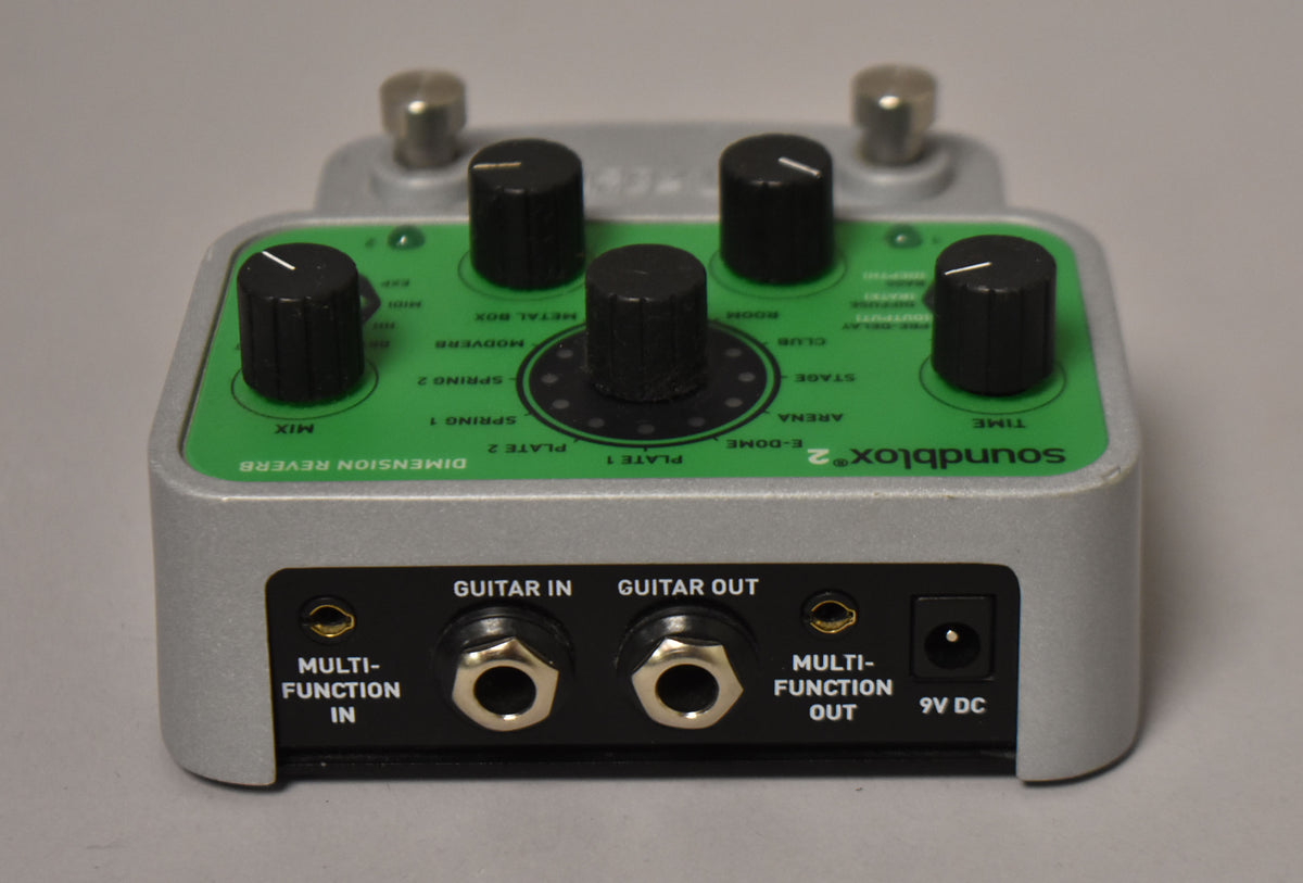 The reverb pedal is shown from a high angle, revealing its silver casing, green faceplate with five black knobs, and rear input/output jacks.