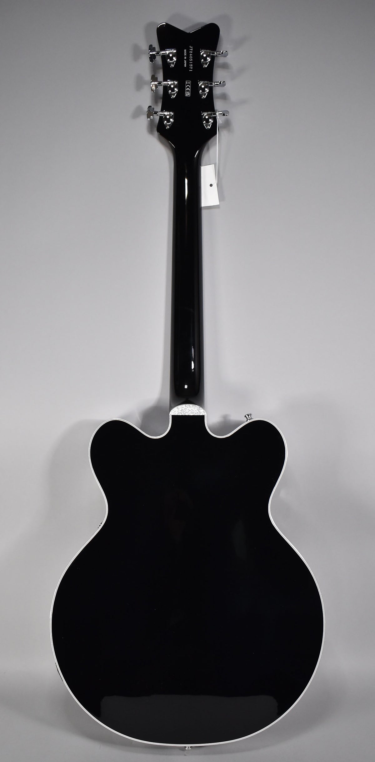 The guitar's glossy black back and neck are visible, with a white binding outlining the body and headstock, which has six chrome tuners.