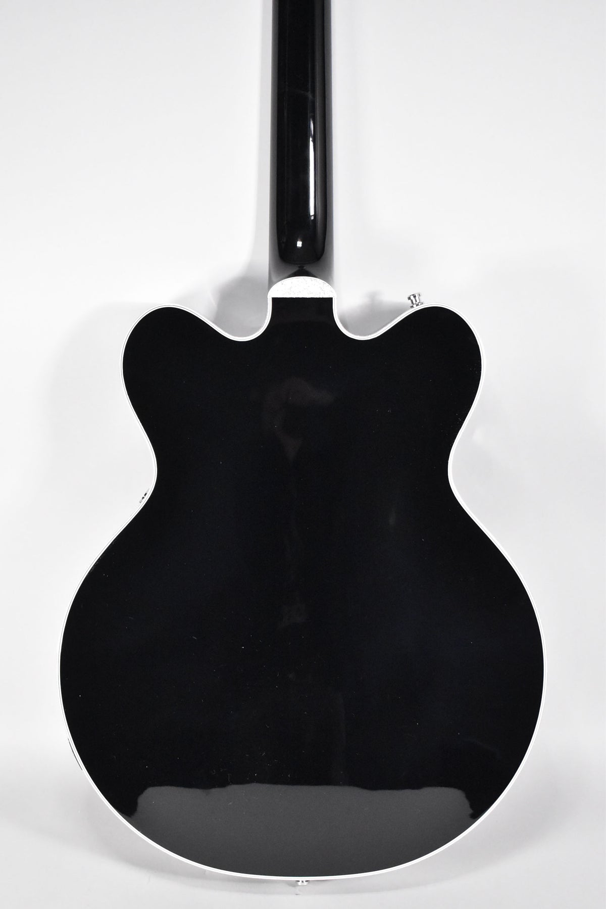 The back of a glossy black hollow-body electric guitar with white binding, showing the neck joint and strap button.