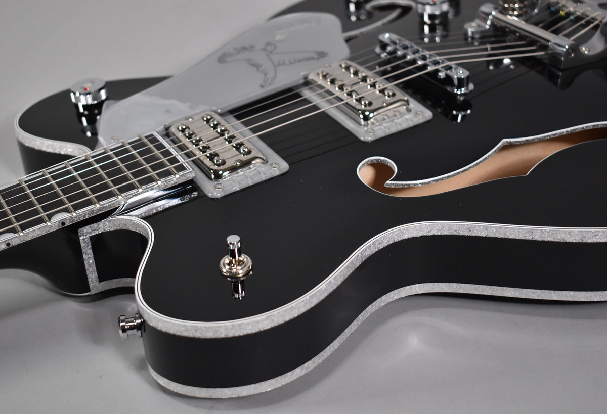 Close-up of a glossy black hollow-body electric guitar with silver sparkle binding, chrome hardware, and a silver pickguard.