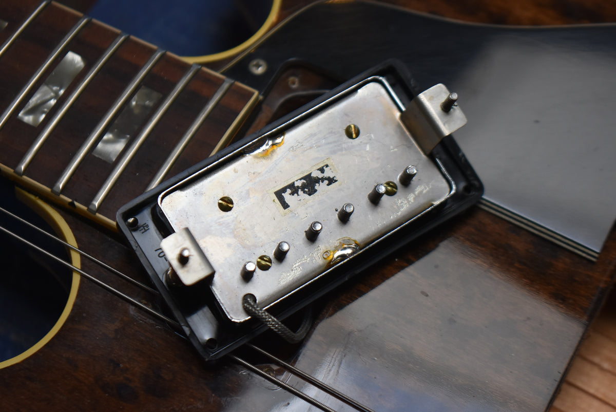 Close-up of the guitar's bridge pickup, showing its tarnished metal cover, exposed pole pieces, and some wear on the walnut finish.