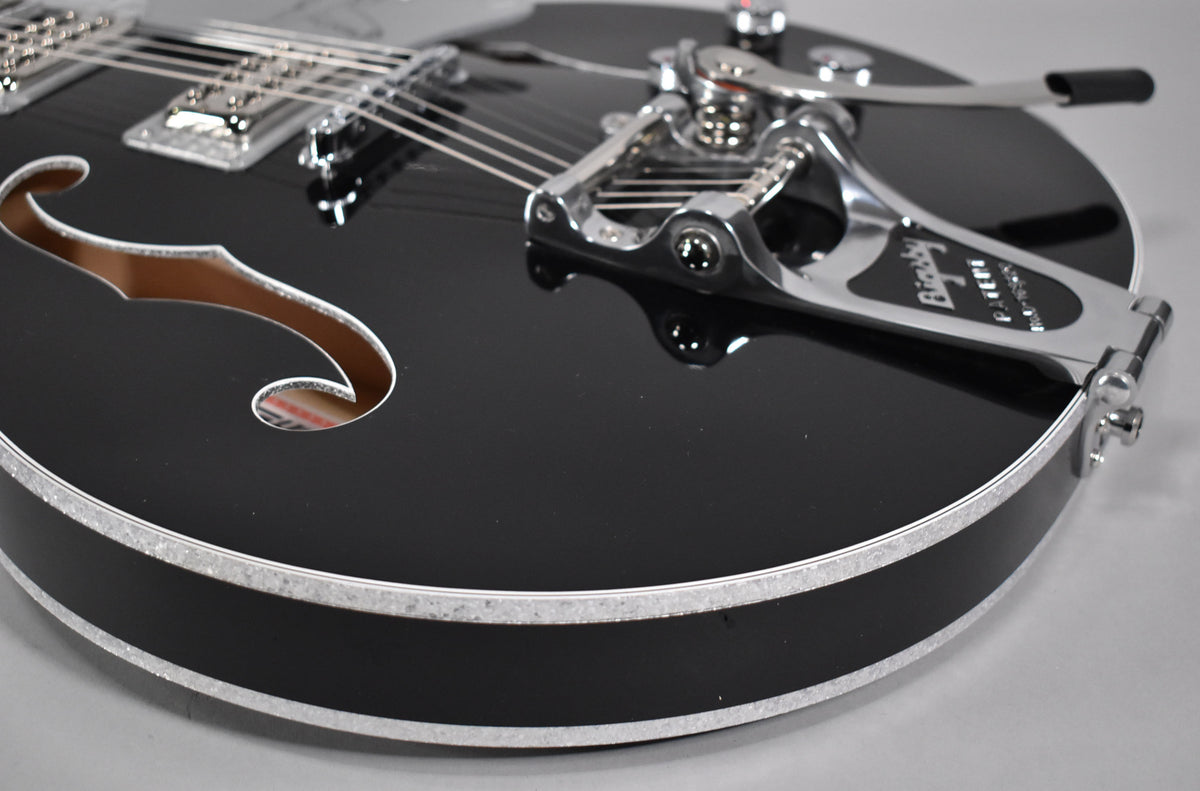 Close-up of the black guitar's lower bout, showing the f-hole, chrome Bigsby vibrato, and silver sparkle binding.