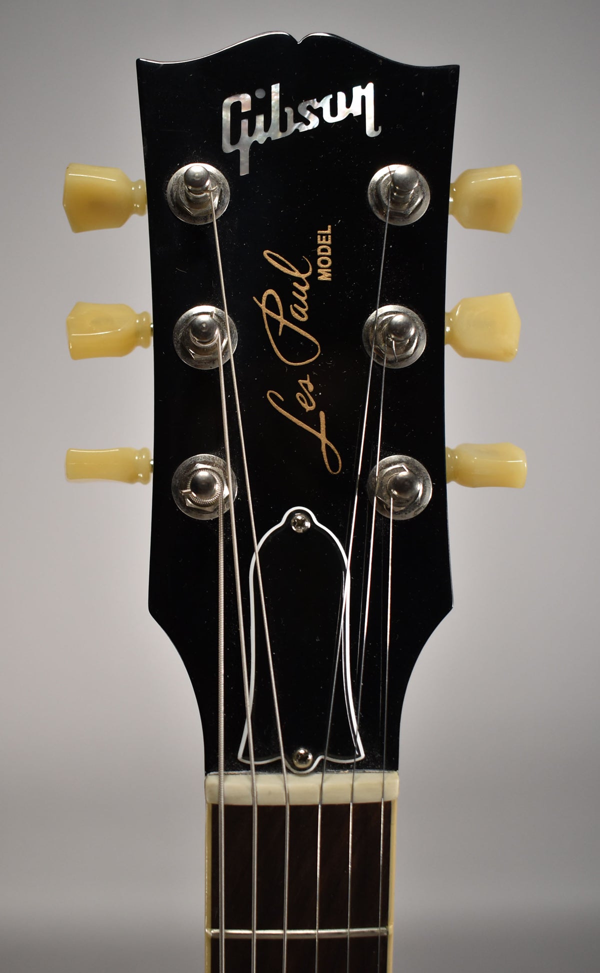The black headstock, with cream tuning pegs and a bell-shaped truss rod cover, is viewed from the front.