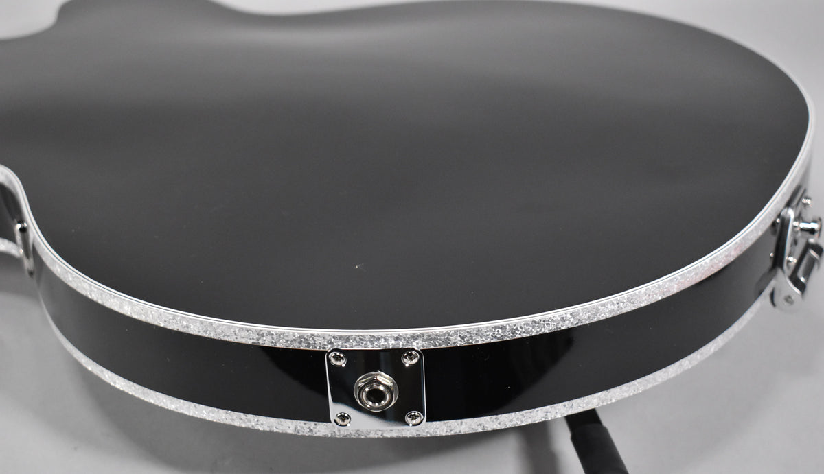 Close-up of the guitar's lower bout, showing the black gloss finish, silver sparkle binding, and chrome output jack on the side.