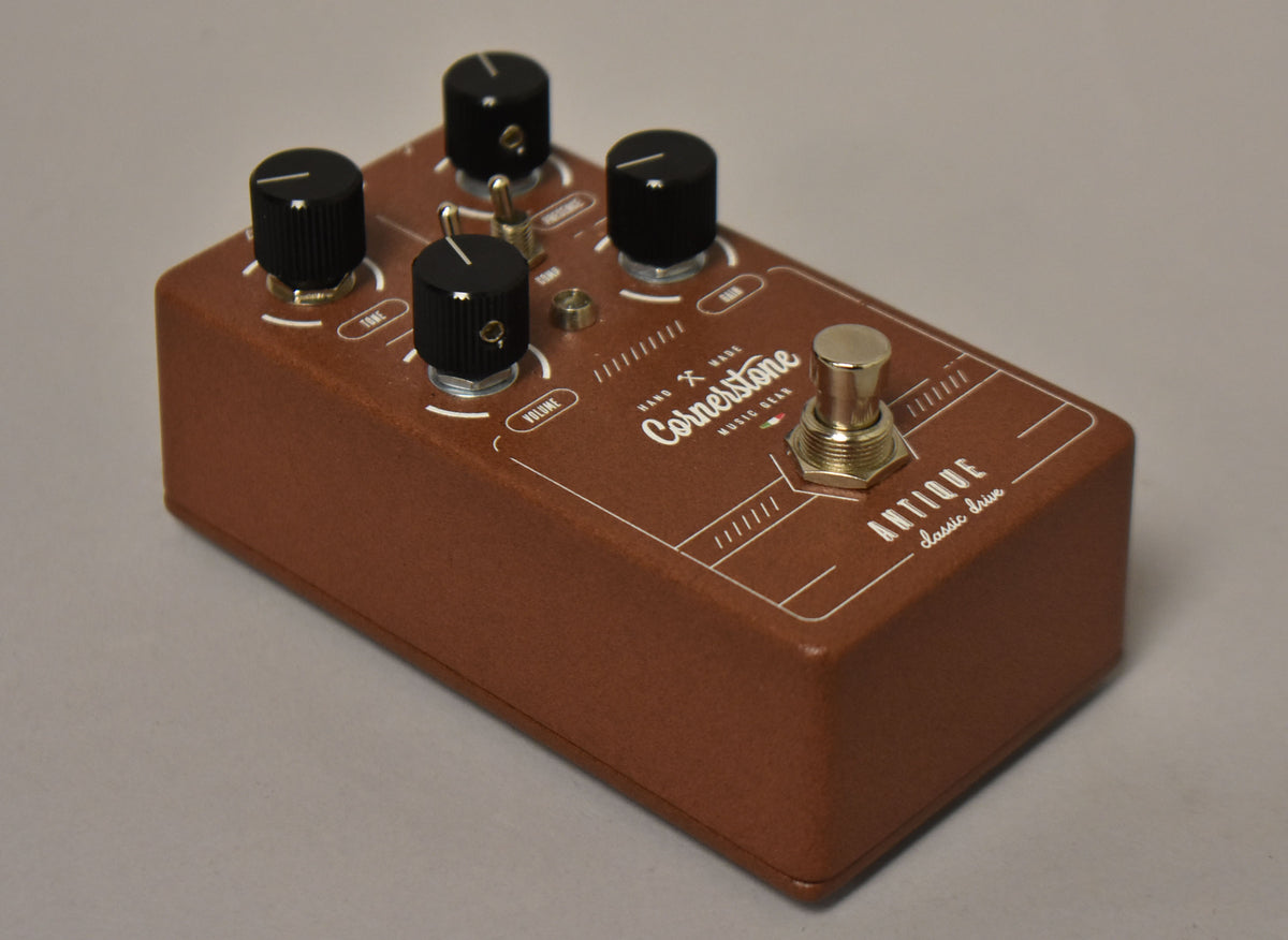 A brown textured pedal, angled from the front right, with four black knobs, a toggle switch, and a gold footswitch.