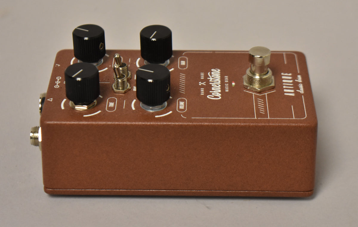 A brown textured pedal, angled from the left, shows four black knobs, a silver toggle switch, and a silver footswitch.