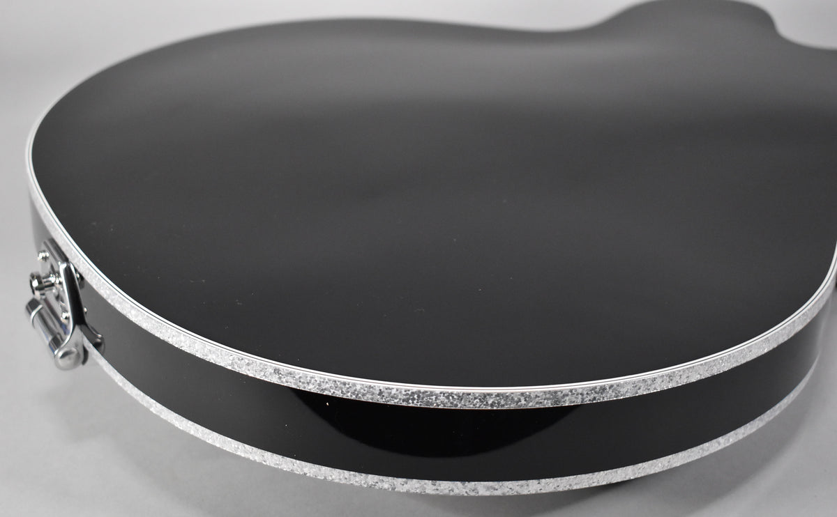 The guitar's glossy black body, with silver sparkle binding on the top and bottom edges, is viewed from the lower bout.