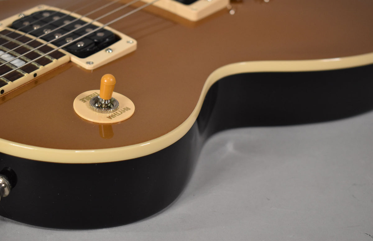 Close-up of the guitar's upper body, showing the goldtop finish, cream binding, black sides, and a cream rhythm/treble switch.