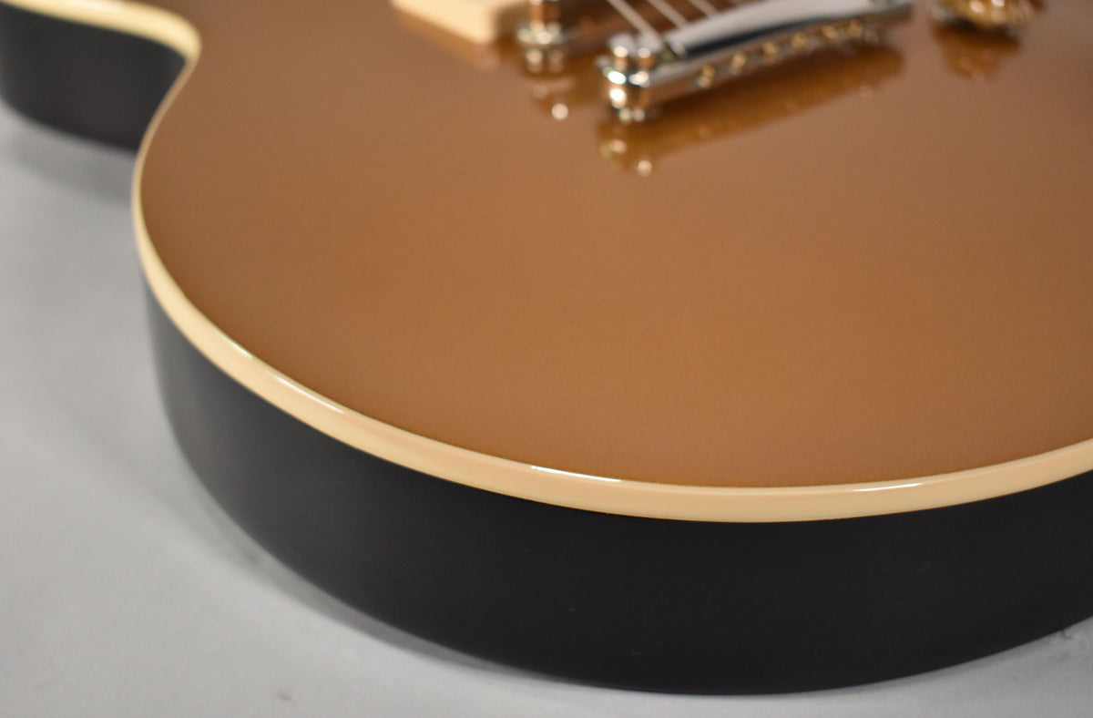 Close-up of the guitar's lower bout, showing the metallic gold top, cream binding, and matte black sides.