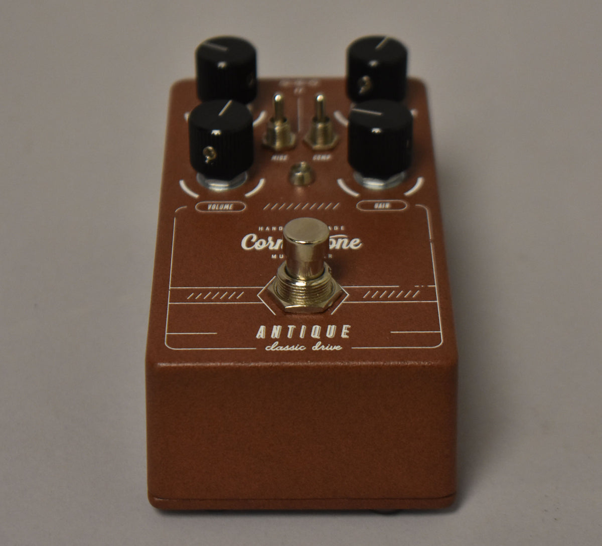 Brown pedal with a textured finish, four black knobs, two gold toggle switches, and a gold footswitch, viewed from the front.