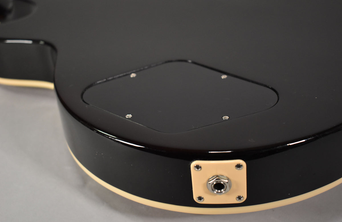 Close-up of the guitar's black gloss back, showing the control cavity cover and the cream-colored output jack plate with chrome jack.