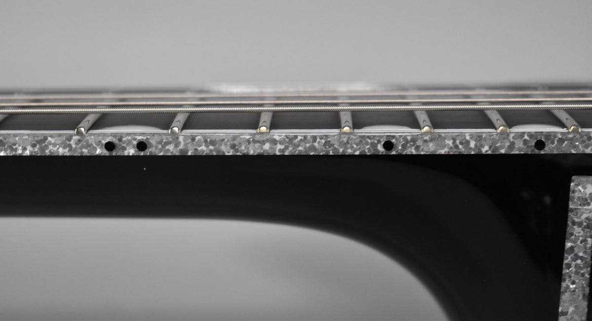 Close-up of the guitar's black body and silver sparkle binding, with strings and frets visible from a low angle.