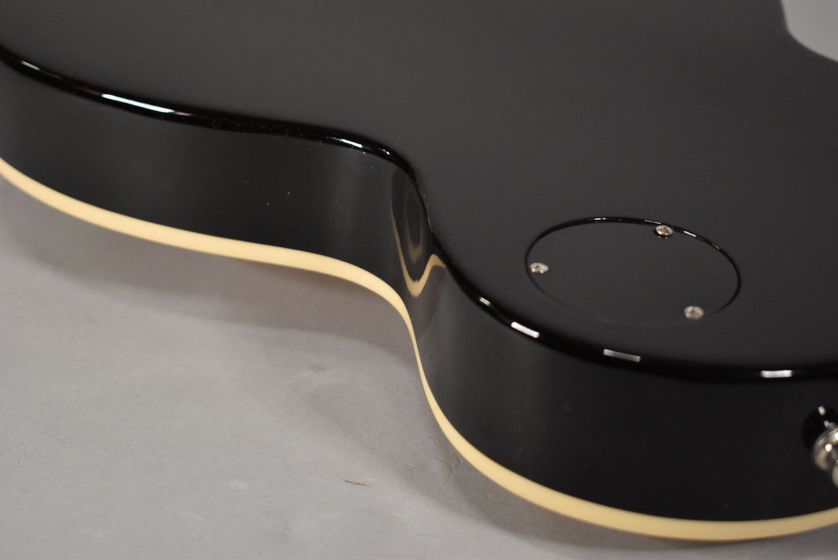 Close-up of the guitar's lower bout, showing the black gloss finish, cream binding, and the circular control cavity cover on the back.