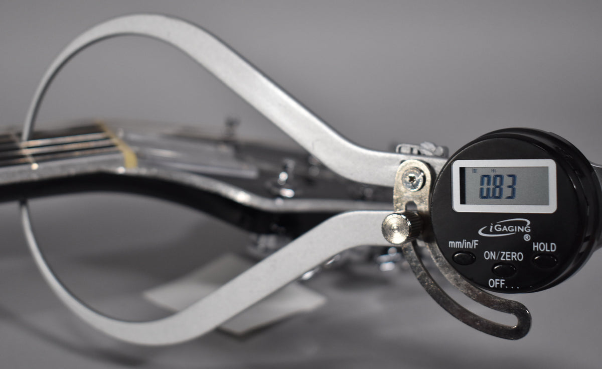 A digital caliper measures the string height at the nut of the black guitar, displaying 0.83mm.