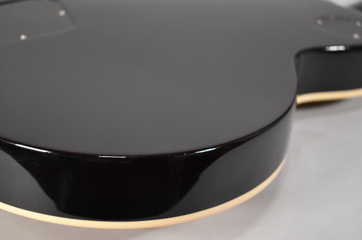 Close-up of the guitar's lower bout, showing the glossy black back and sides with cream binding, and a few minor surface scuffs.