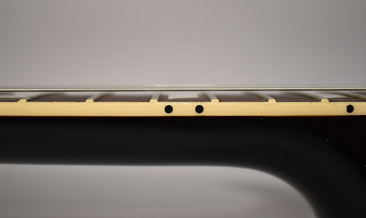 Close-up of the guitar's dark neck and cream binding, showing two black side dot markers and three strings over the fretboard.