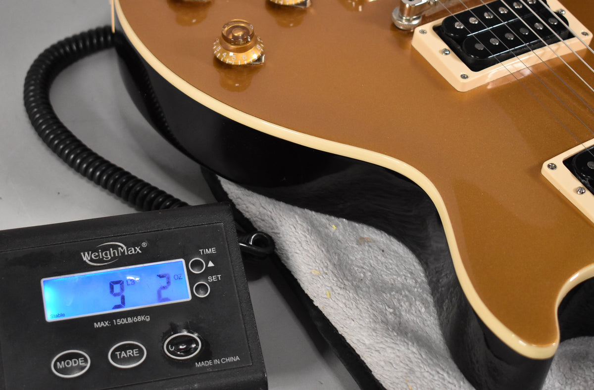 Close-up of the guitar's goldtop body and black sides, showing a digital scale displaying "9 lbs 2 oz" in the foreground.