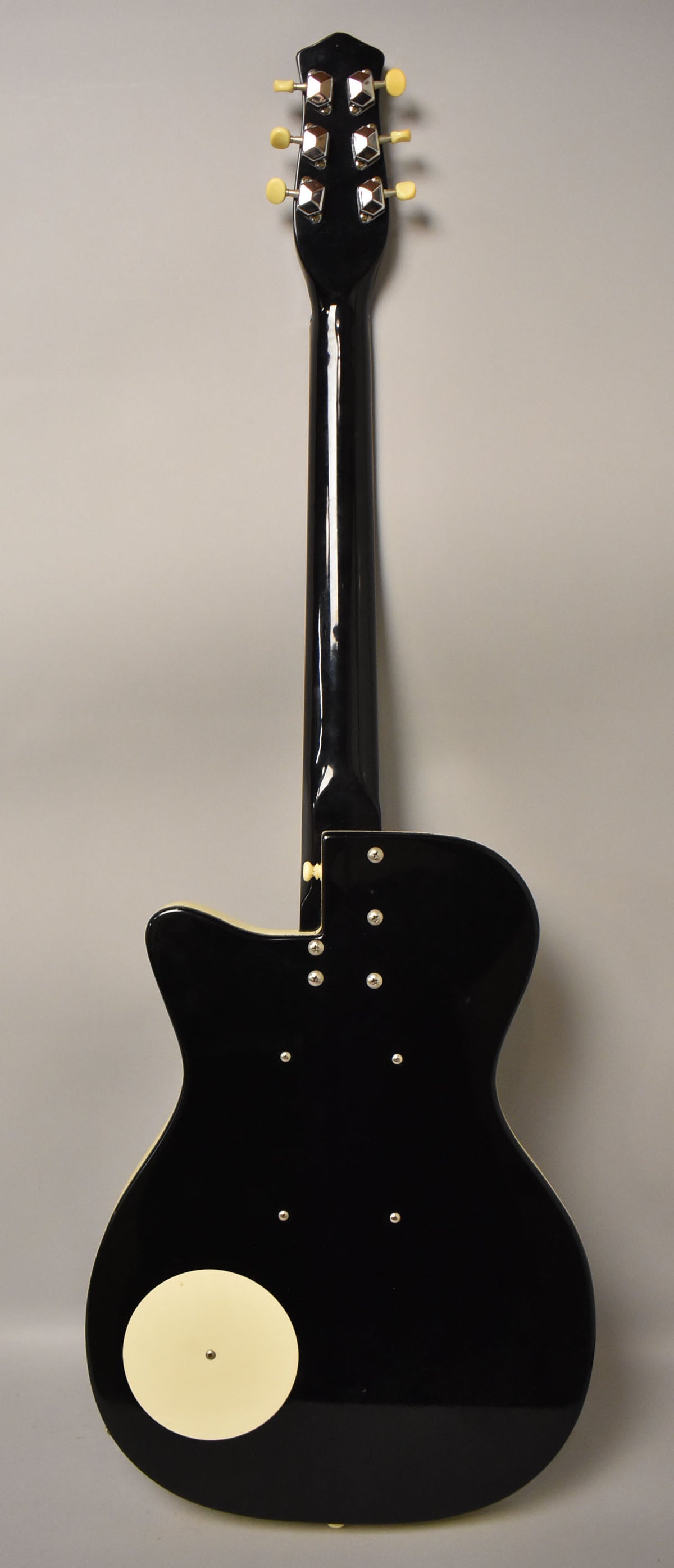 The guitar's glossy black back, neck, and headstock are shown, with six chrome tuners and a cream circular control plate.