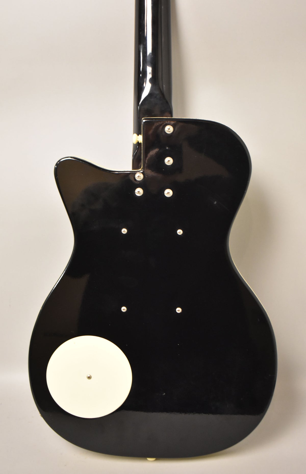 The guitar's glossy black back shows light scratches, a white circular cover, and a neck plate with four screws.