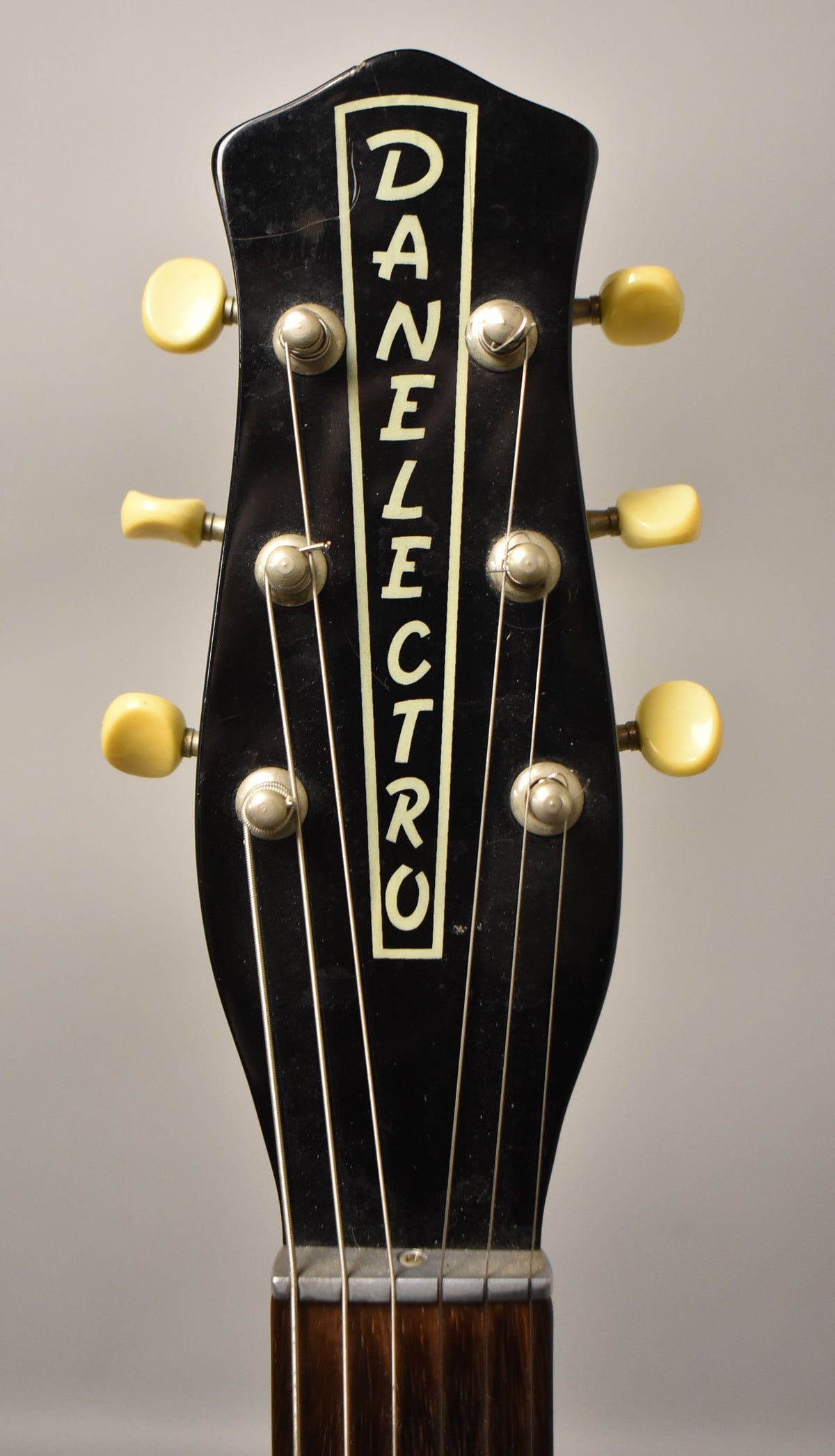 Close-up of the black headstock with six cream tuning pegs, showing light wear and dust, and the top of the dark fretboard.