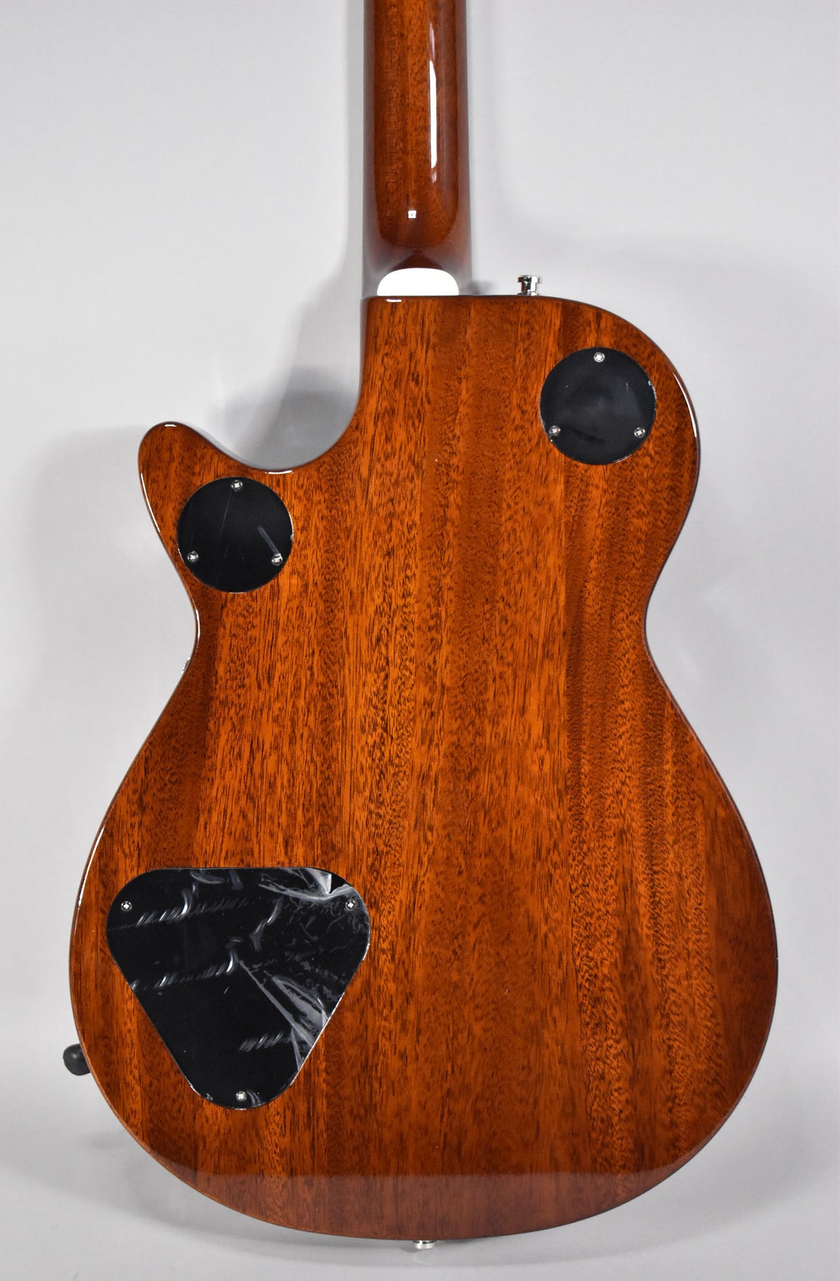 The guitar's mahogany back and neck are visible, with three black control cavity covers, one still with protective film.