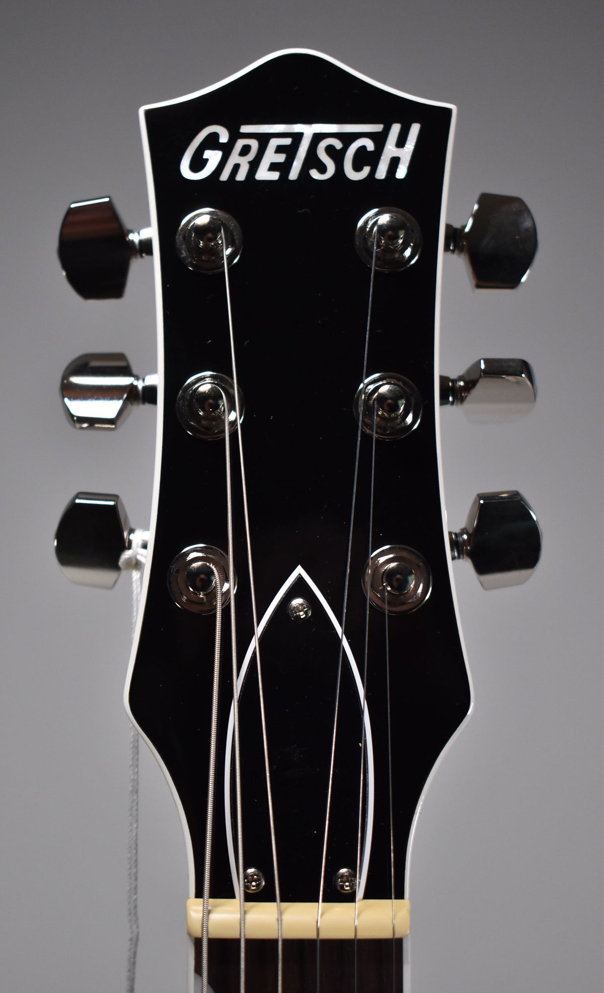 Close-up of the black headstock with white binding, showing six chrome tuners, a bone nut, and the top of the fretboard.