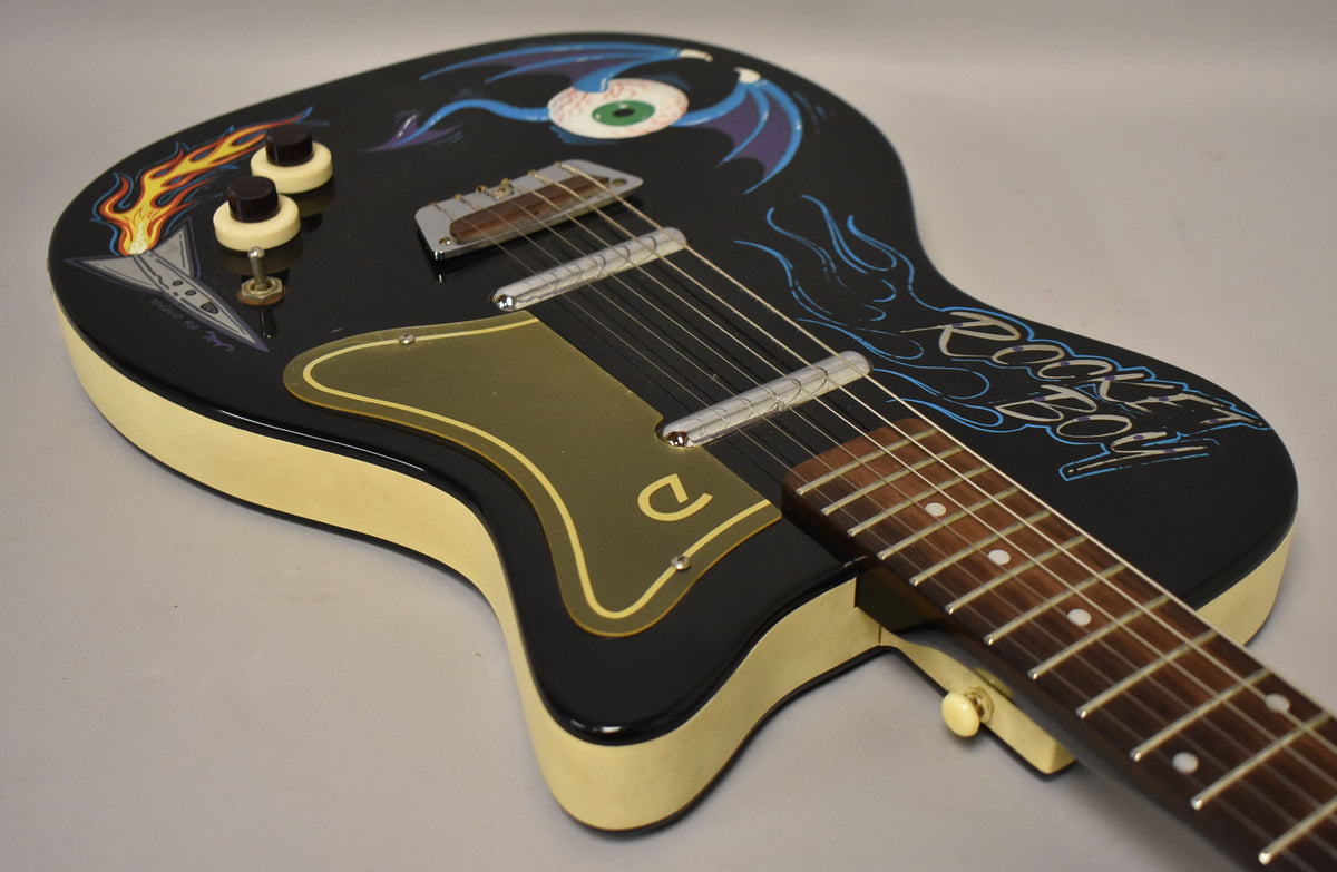 The black guitar body, with cream sides, is angled from the upper left, showing custom flame, eyeball, and "Rocket Boy" paint.