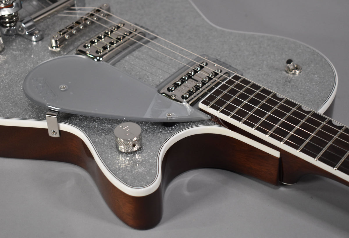 Close-up of the guitar's lower bout, showing the silver sparkle finish, clear pickguard, chrome hardware, and dark wood neck.