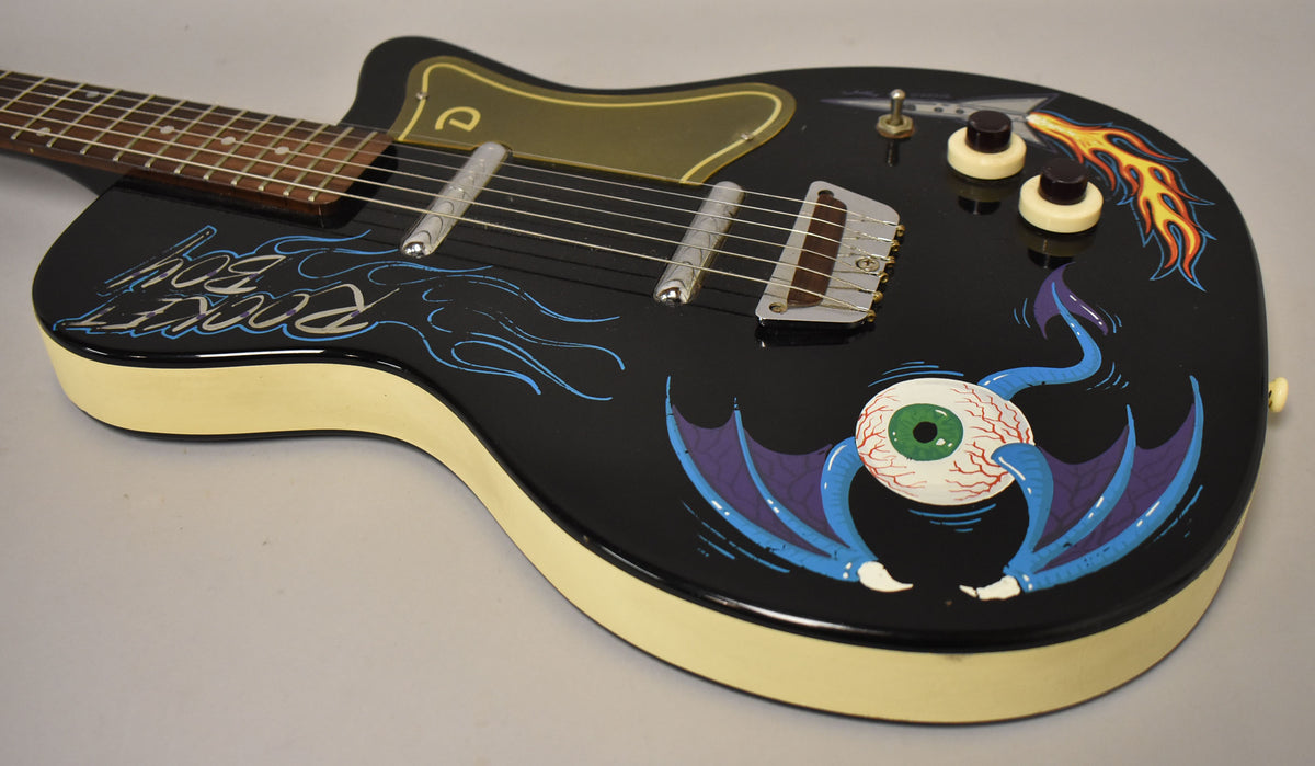 The black guitar body, with cream sides, is angled from the neck to the lower bout, showing custom flame and eyeball art.