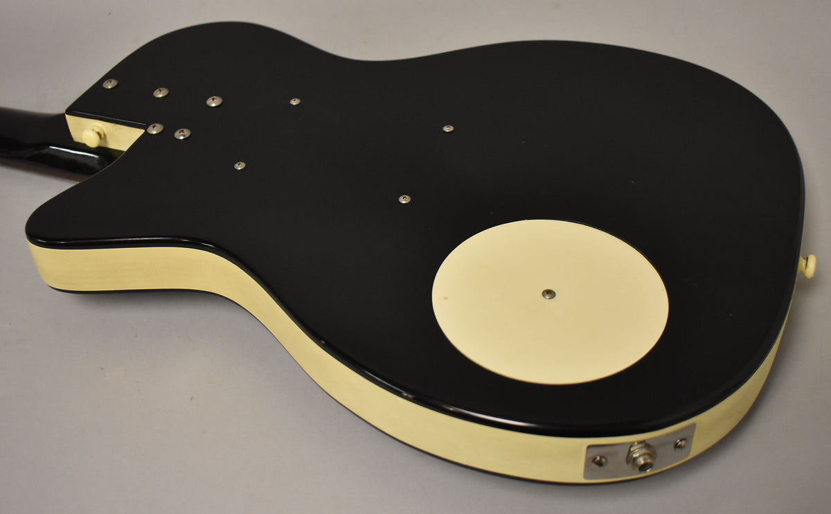 The guitar's black matte back and cream sides are visible, with a cream circular cover and chrome output jack.