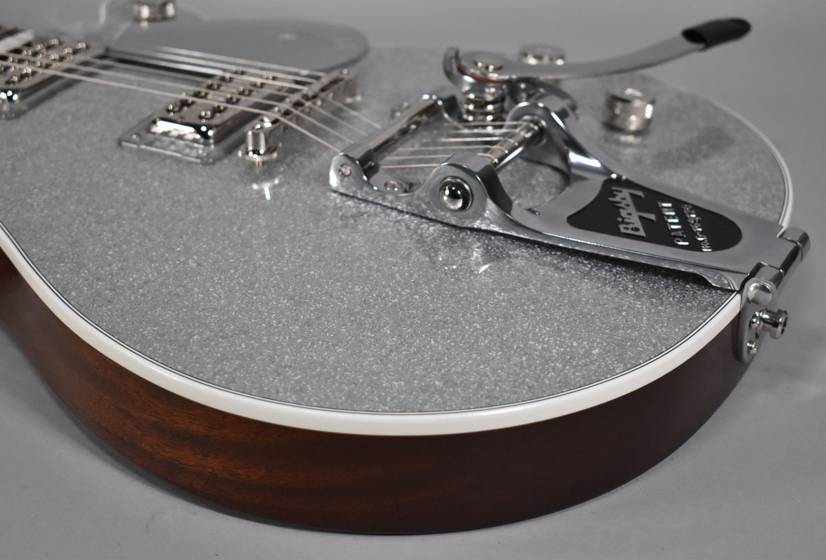 Close-up of the silver sparkle guitar body, showing the Bigsby vibrato system, chrome hardware, and dark brown sides with white binding.