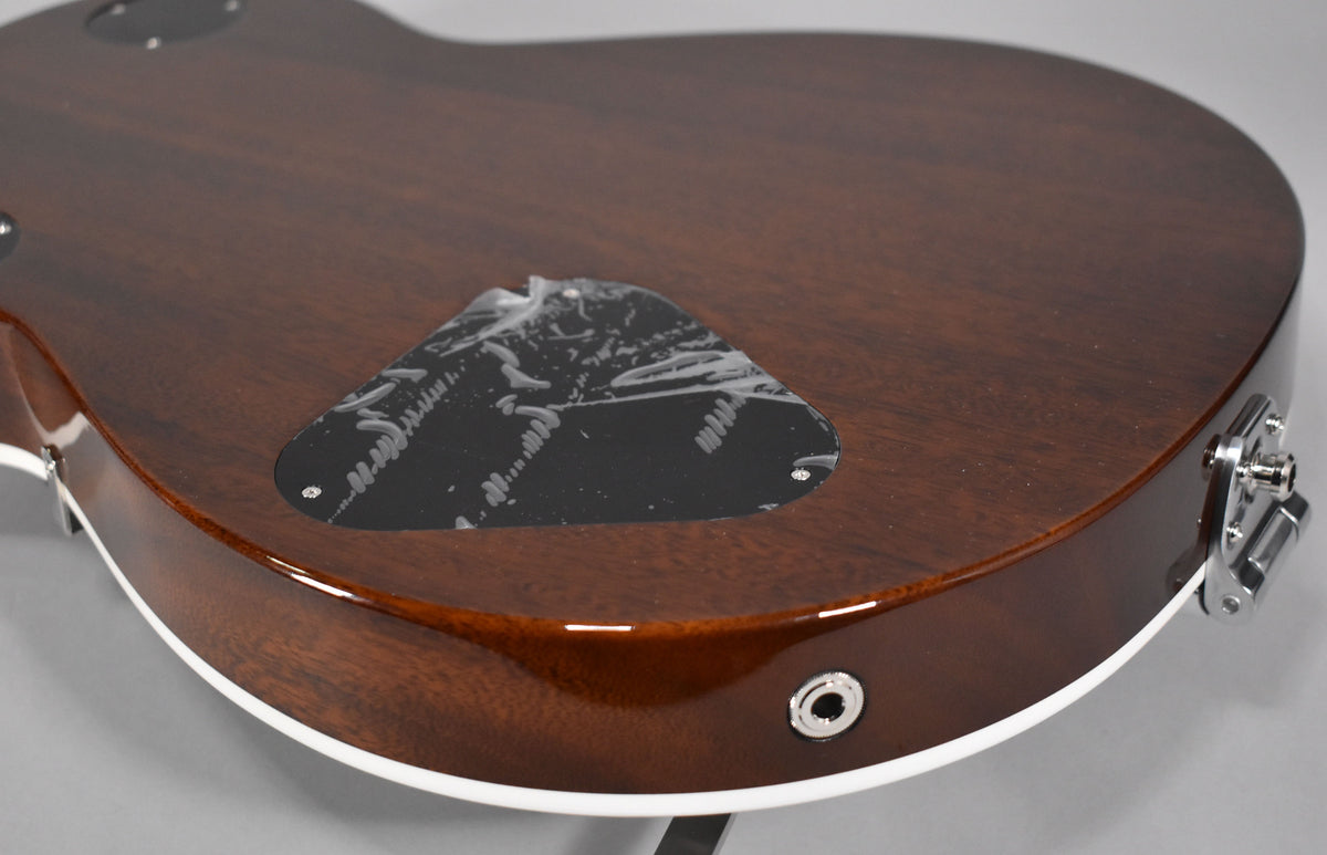 The guitar's dark brown back and side are visible, with a black control cavity cover still bearing its protective film.