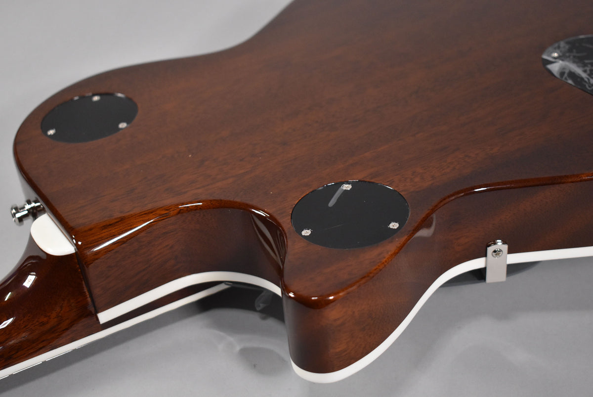 The guitar's dark brown back and sides are visible, with two black control cavity covers and white binding along the edges.