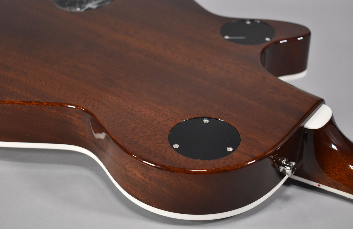 The guitar's dark brown back and sides, with white binding, show two black circular control plates and a chrome output jack.